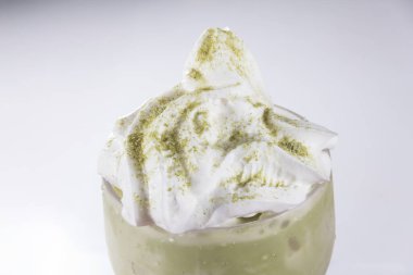 Üzerinde krem şanti ve yeşil çay tozu olan uzun bir bardak buzlu matcha latte, temiz beyaz bir arka planda fotoğraflanmış..