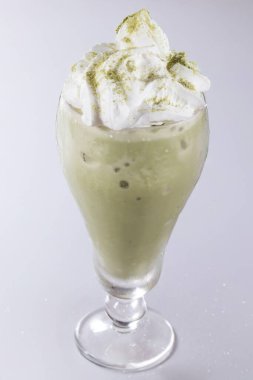 Havadar krem şanti ve kibrit tozu ile taçlandırılmış büyük bir bardak buzlu kibrit sütlü latte..