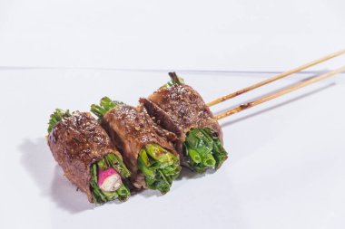 Üç şişe ızgara sığır eti yeşil sebzelere sarılmış, lezzetli ve dumanlı..