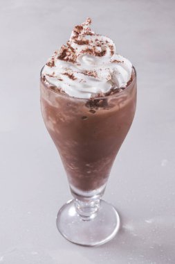 Krem şanti ve kakao tozu serpiştirilmiş uzun bir bardak çikolatalı milkshake..