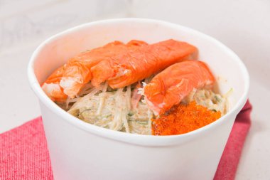 Yengeç çubukları ve parlak turuncu kabuklu süslemelerle kaplı kremalı salata dolu beyaz bir kase..