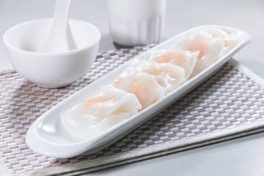 Uzun beyaz bir tabak buğulanmış pirinç rulosu. Karidesle doldurulmuş, sosla servis edilmiş..