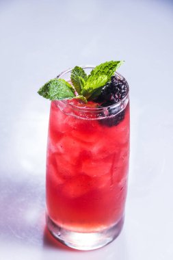 Buzlu, nane yapraklı ve böğürtlen garnitürlü uzun bir bardak kırmızı meyve çayı..