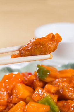 Arka planda dolmalık biberler ve ananas parçalarıyla birlikte yemek çubuklarının tuttuğu tatlı ve ekşi bir parça domuz eti..