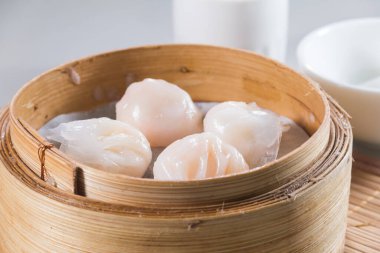 Narin karides köfteleriyle dolu bambu bir buhar tenceresi, yakınlarda beyaz kâselerle dokunmuş bir hasırın üzerine yerleştirilmiş..