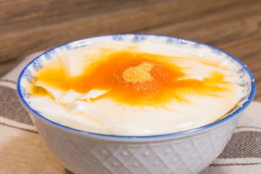 Altın şurup ve şeker tozuyla kaplı pürüzsüz fasulye kaymağı dolu çiçek desenli bir kase..