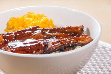 Izgara yılan balığı filetosu ve dilimlenmiş yumurtayla kaplı buğulanmış pirinçle dolu beyaz bir kase..