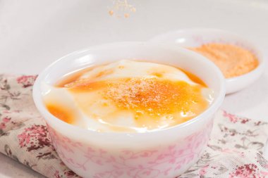 Altın şurup ve şeker tozuyla kaplı bir kase pürüzsüz soya peyniri. Çiçek bezine konmuş..