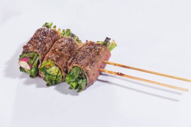 Üç şişe ızgara sığır eti taze yeşil sebzelere sarılıp beyaz kağıda servis ediliyor..