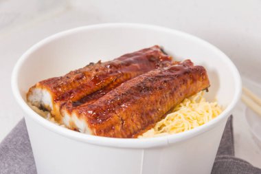 İki ızgara yılan balığı fileto ve dilimlenmiş yumurta ile kaplı buğulanmış pirinçle dolu beyaz bir kase..