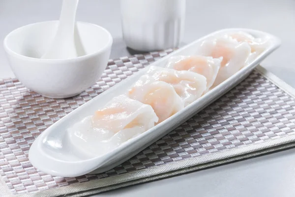 Uzun beyaz bir tabak buğulanmış pirinç rulosu. Karidesle doldurulmuş, sosla servis edilmiş..