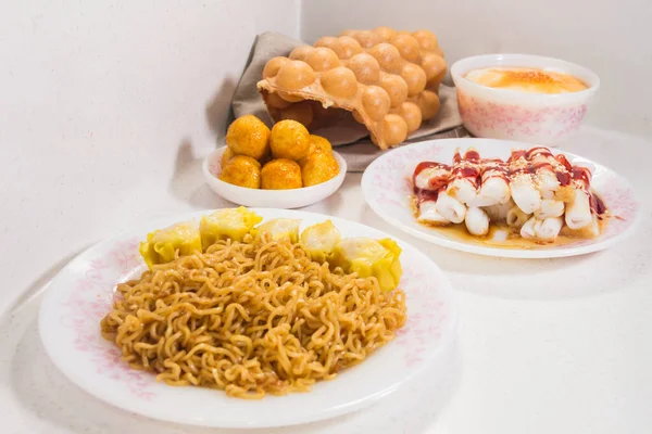 Siu mai, yumurta waffle, balık köftesi ve soslu pilav ile servis edilen bir tabak kızarmış erişte..