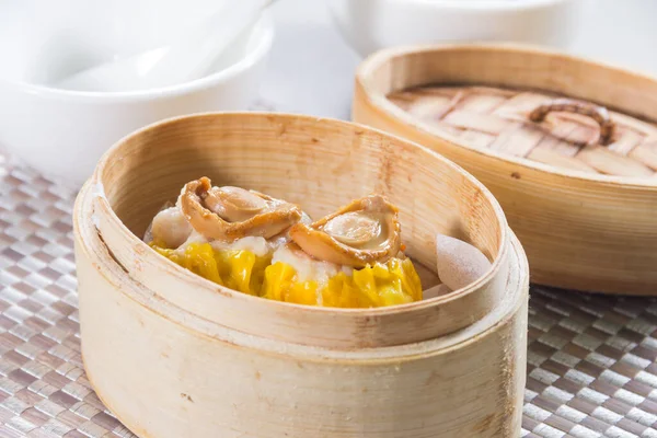 Üzerinde küçük deniz kulağı parçaları olan iki siu mai hamur tatlısı olan bambu budan bir buhar tenceresi..