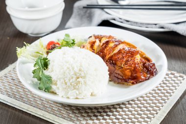 Kızarmış tavuk buğulanmış pirinç ve taze garnitürle servis edilen beyaz bir tabak..