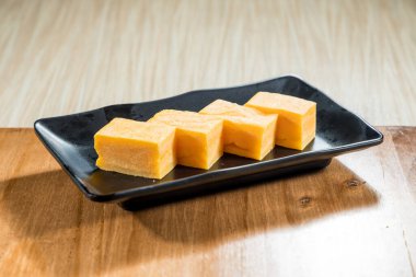 Beş dikdörtgen Japon Tamagoyaki dilimi siyah bir seramik tabağa yerleştirilmiş..