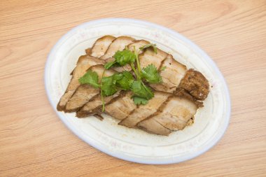 Taze maydanozla süslenmiş domuz eti dilimlenmiş oval bir tabak..