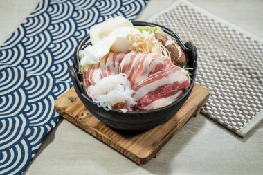İçinde domuz dilimleri, tofu ve mantar içeren Shabu Shabu malzemeleriyle dolu siyah bir tencere..