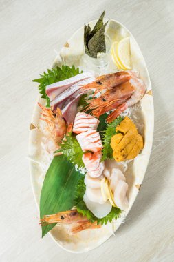 Karides, somon, deniz kestanesi ve deniz kestanesi içeren çeşitli sashimi içeren büyük bir oval tabak..