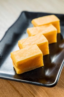 Dört dikdörtgen Japon tamagoyaki yumurta rulosu siyah seramik bir tabakta güzelce dizilmiş..
