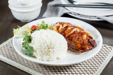 Kızarmış tavuk dilimleri sunan beyaz bir tabak. Buharda pilav ve taze salata garnitürle servis ediliyor..