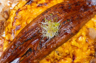 Altın yağda yumurtalardan oluşan bir yatağın üstüne konmuş, üstünde garnitür olan, yakın plan ızgara yılan balığı..