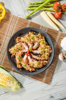 Bambu hasırında servis edilen sarımsak ve yeşil otlarla çevrili yuvarlak bir karides tabağı..