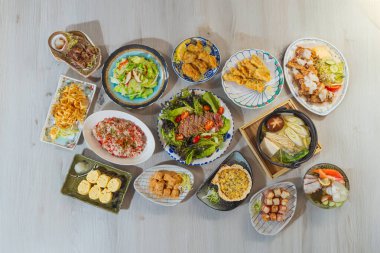 A large spread of Japanese dishes including sushi, tempura, salad, and hot pot arranged on a wooden table for a traditional meal.