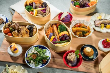 Izgara et, sebze ve rengarenk kenarlarla dolu bir sürü bento kutusu. Zarif bir Japon sunumu için ahşap tepside dizilmiş..