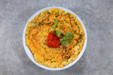 Üzerinde kırmızı sos ve gri bir yüzey üzerinde taze kişniş bulunan beyaz bir kasede servis edilen altın bir omlet..