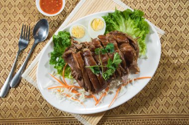 Bir tabak haşlanmış yumurta, marul ve ezilmiş sebzeyle servis edilen domuz budu dilimleri..