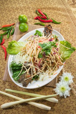 İnce dilimlenmiş sebze ve otlarla kaplı, kireç ve biberli süslemeli ve desenli bir hasırla servis edilen bir tabak çıtır balık..