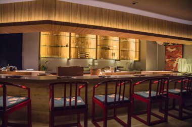 Ahşap rafları, cam vitrinleri ve tezgah boyunca dizilmiş kırmızı sandalyeleri olan modern bir restoran barı..