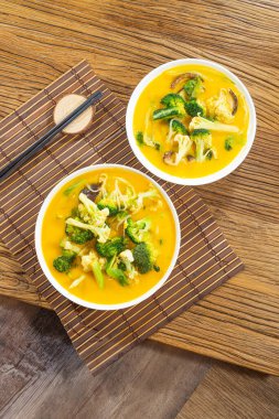 Üzerinde brokoli çiçekleri ve mantarlar olan iki kase kremalı balkabağı çorbası bambu hasırında servis edilir..