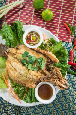 Marul ve doğranmış havuçlardan oluşan bir yatağa yerleştirilmiş tam bir kızarmış balık, desenli masa örtüsüne batırılmış soslarla servis ediliyor..