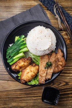 Buharda pilav, kızarmış tavuk kanadı, domuz dilimleri ve taze yeşillikler içeren siyah bir tabak..