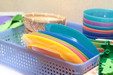 İçerideki sepete yerleştirilmiş renkli plastik tabak ve kaseler..