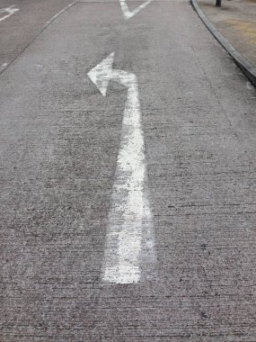 Kaba beton bir yol yüzeyine gün ışığında beyaz bir ok çizilmiş..