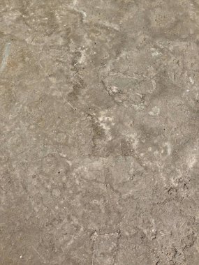 Görünür izler ve düzensiz desenlerle gri beton bir zeminin yakın görüntüsü.