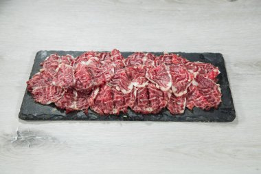 Siyah bir tabaktaki ince dilimlenmiş çiğ et..