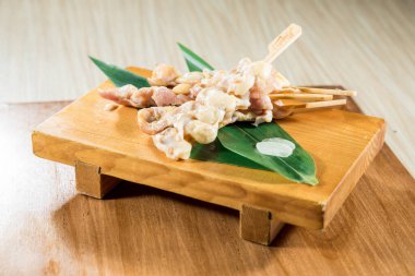 Tahta tepside yeşil yapraklı birkaç çiğ tavuk şişi var..