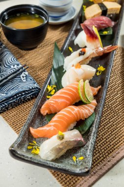 Somon, ton balığı ve deniz tarağı içeren çeşitli suşi parçalarıyla dolu uzun bir dikdörtgen tabak..