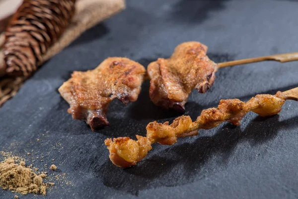 İki ızgara tavuk şiş üzerine baharat serpiştirilmiş siyah bir levhada servis edilir..