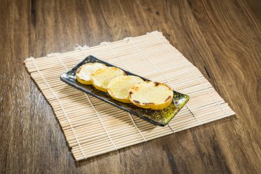 Dikdörtgen siyah bir tabak, bambu bir paspasın üzerine yerleştirilmiş dört altın ızgara patates dilimi barındırır..