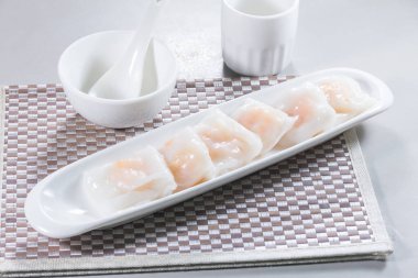 Uzun beyaz bir tabak buğulanmış pirinç rulosu. Karidesle doldurulmuş, sosla servis edilmiş..