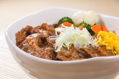 Izgara sığır eti dilimleri, dilimlenmiş yumurta, brokoli ve havuç garnitürle dolu buğulanmış pirinçle dolu beyaz bir kase..