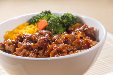 Teriyaki soslu pilav, brokoli, havuç ve doğranmış yumurta ile dolu beyaz bir kase..