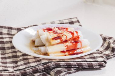 Bir tabak buğulanmış pirinç rulosu üzerine tatlı sos serpilmiş ve susam tohumları serpilmiş..