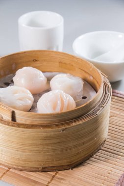 Bambu tenceresi, arka planda beyaz kaseler bulunan bambu hasırına yerleştirilmiş karidesli hamur köfteleriyle dolu..