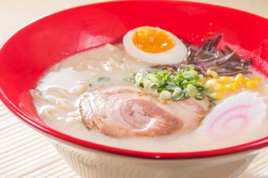 Kırmızı bir kase kremalı ramen çorbası dilimlenmiş domuz eti, yarı haşlanmış yumurta, mısır ve yeşil soğanlı garnitür..