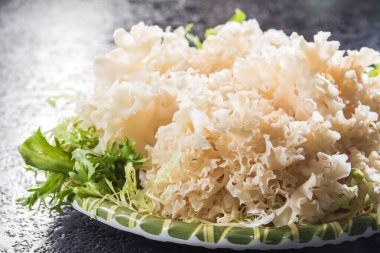 Yeşil yapraklı garnitürle desenli siyah bir yüzeye yerleştirilmiş bir tabak taze beyaz mantar..